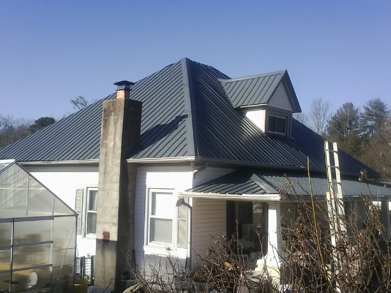 Dark blue standing seam metal roof on a white farmhouse with dormer — Slate & Tile Roof Repair by Roofing Brothers in Bedias
