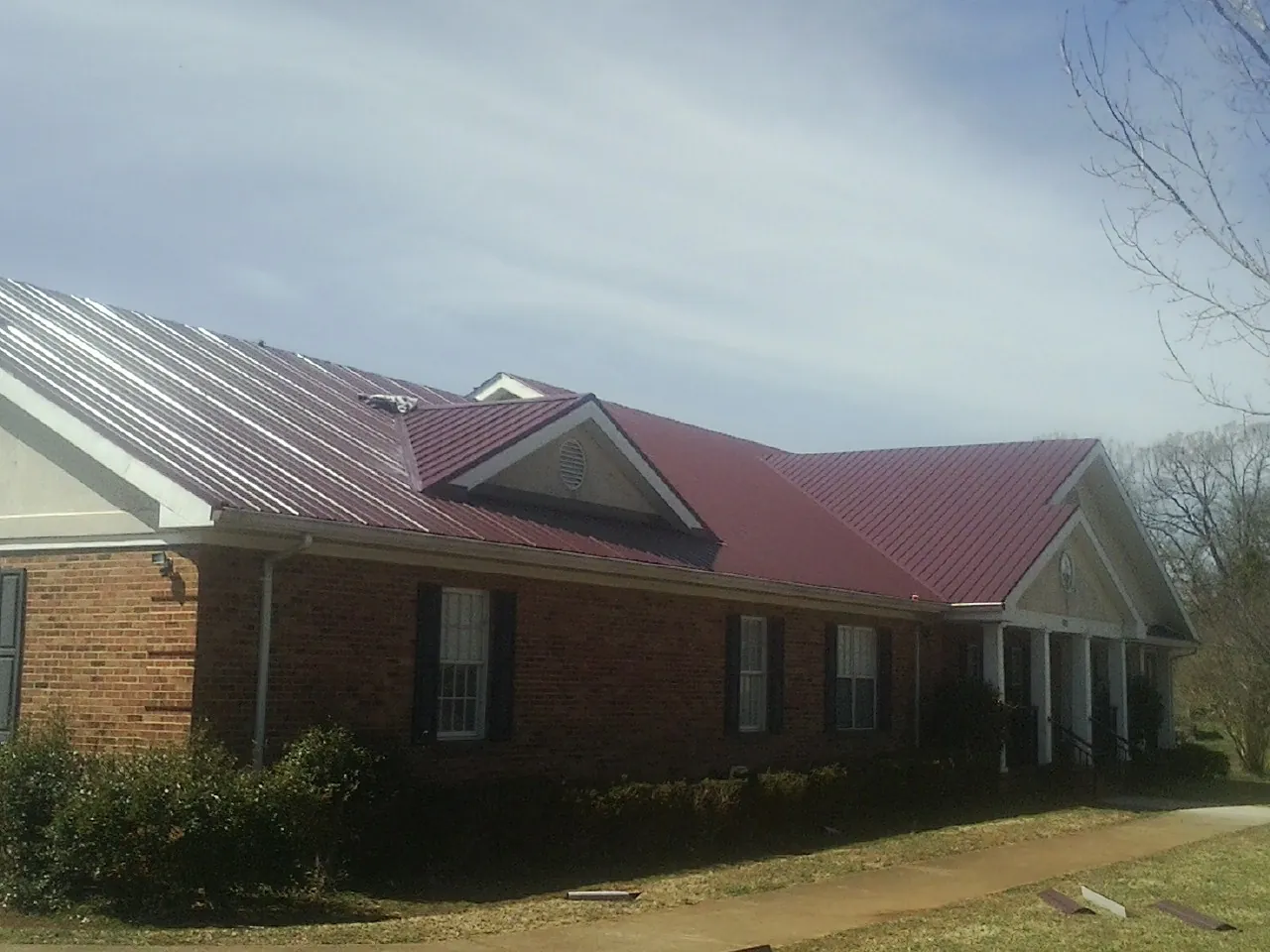Red metal roof with gabled entries on a long brick building, from a Hail Damage Roof Repair job in Bedias