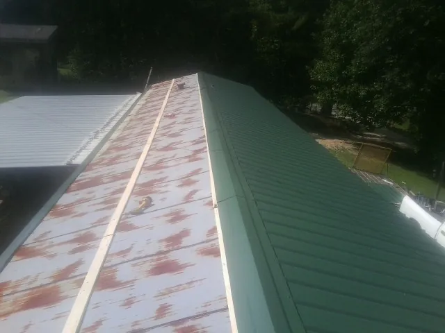 Old rusted panels beside newly installed green metal roofing — Wind Damage Roof Repair by Roofing Brothers in Bedias