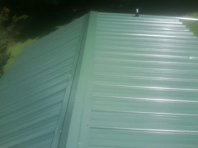 New green metal panels meeting at the ridge of a roof — Flat Roof Repair work by our crew in Bedias