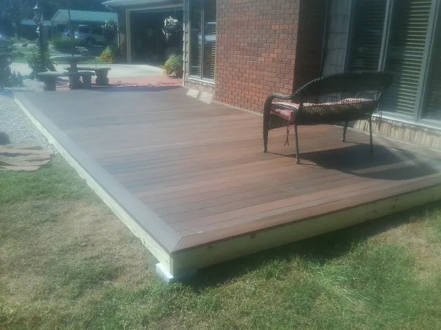 New wood deck and wicker chair beside a brick house in Bedias