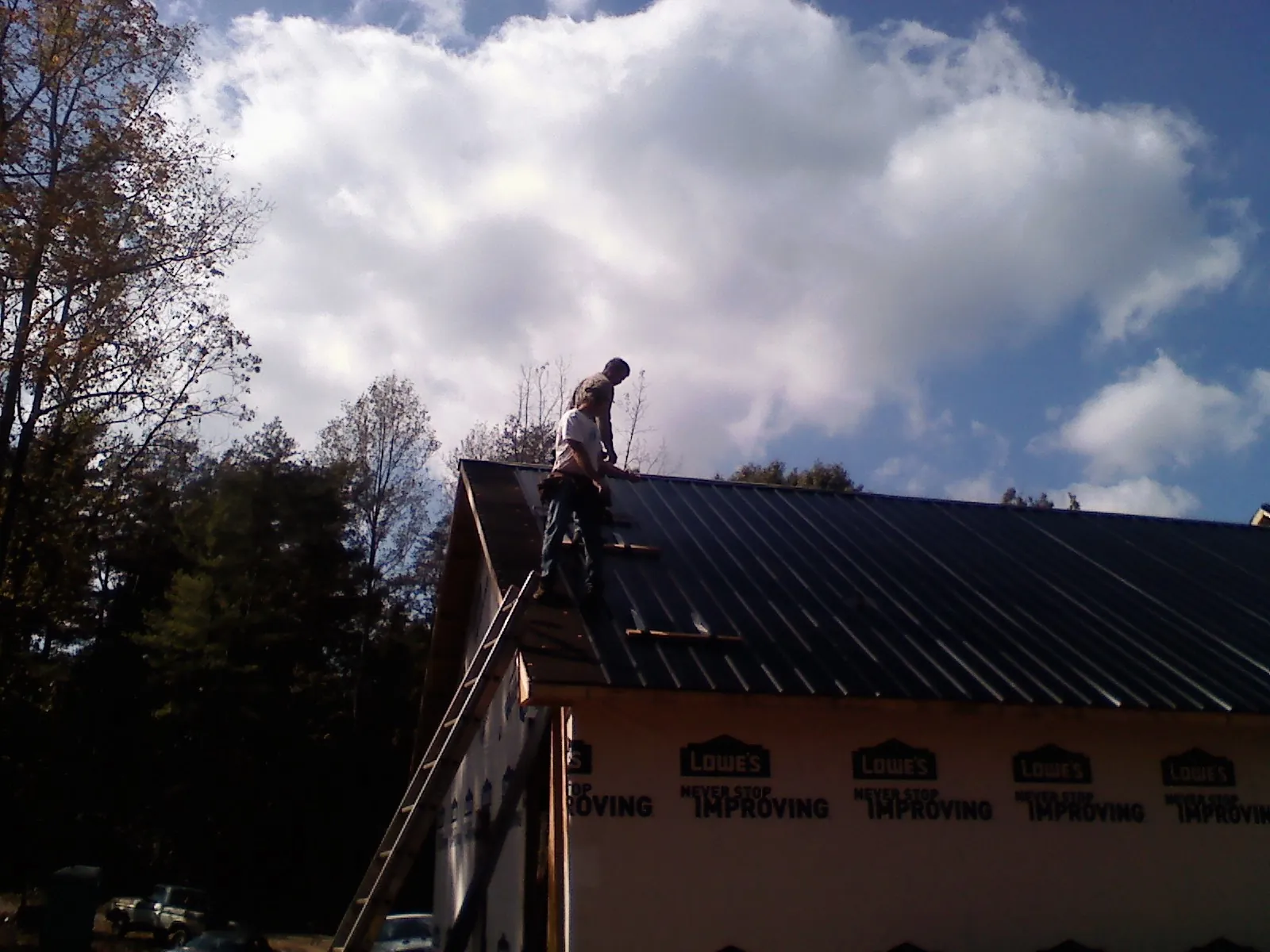 Roofer fastening dark metal panels high against a cloudy sky, from a Roof Inspection job in Bedias