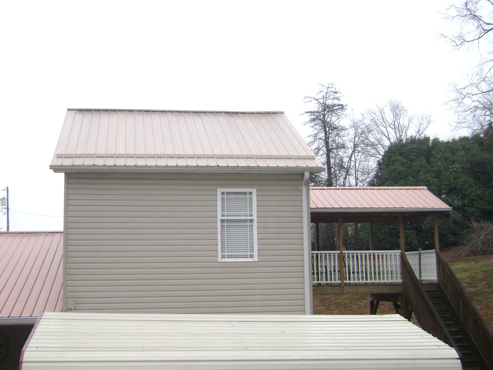 Tan metal roofs on a two story addition and attached porch, from a Roof Replacement job in Bedias